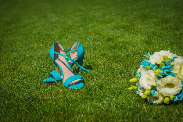 Bouquet di weddong posa all'erba verde adn i sandali in piedi vicino a tutti in colori blu Fotografia Stock
