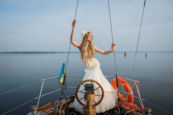 wedding on the sailing yacht . happy bride near the steering wheel, beautiful blonde in wedding dress. blue sky