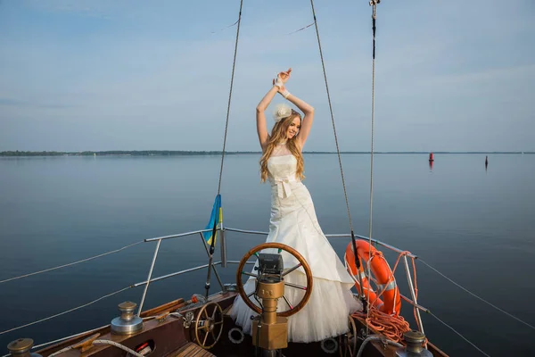 在游艇上的婚礼。在方向盘上，穿着婚纱的美丽金发附近幸福的新娘。蓝蓝的天空 — 图库照片
