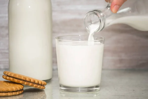 Milk poured into glass from woman hand on wooden background. fresh milk