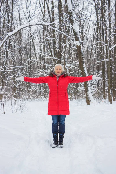 Porträtt av en trevlig äldre kvinna i vinter snö trä i röd kappa — Stockfoto