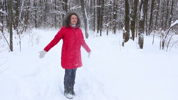 Привлекательная пожилая женщина в зимнем снежном лесу в красном пальто веселится — стоковое видео