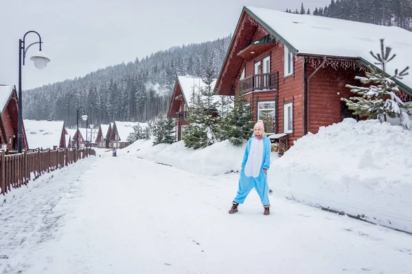 Kız mavi kar dağlarda Kayak rapordaki pembe tek boynuzlu at pijama kigurumi önünde ahşap açık evler.