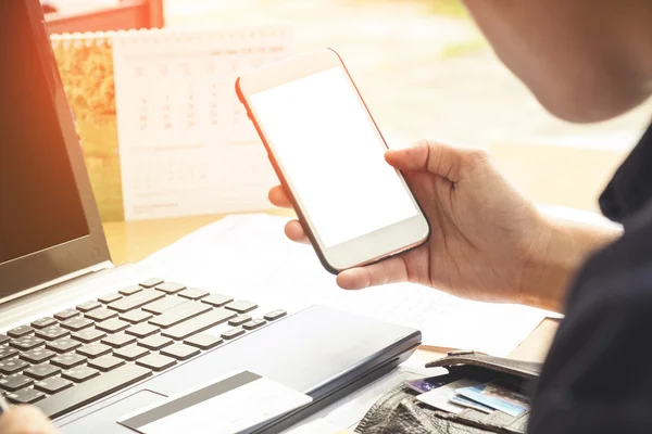 Hand innehav med mobiltelefon med blank skärm och använda Lapt — Stockfoto