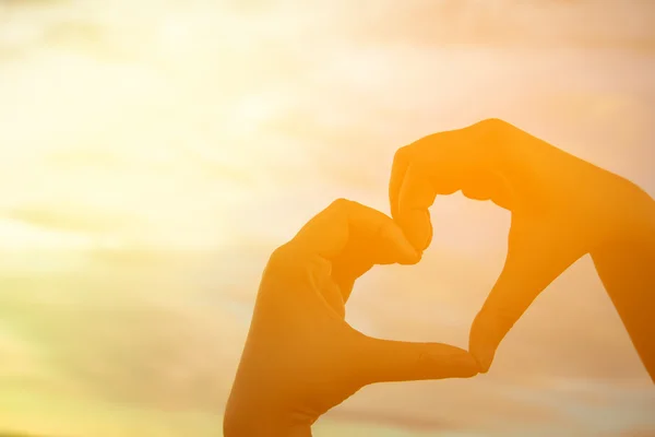 Mãos formando um coração com silhueta do pôr do sol e espaço de cópia — Fotografia de Stock