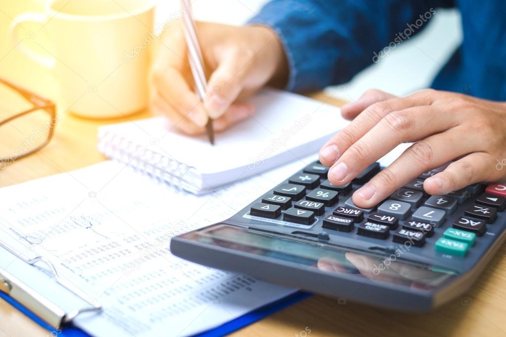 Financial data analyzing hand writing and counting on calculator