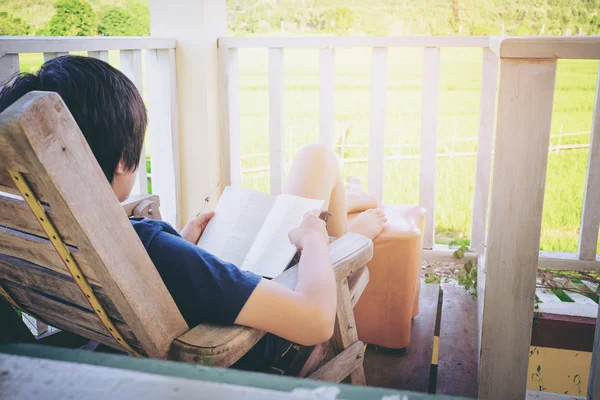 Junger Mann liest ein Buch und liegt im Bett auf der Terrasse mit — Stockfoto