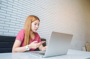 Asyalı kız cep telefonu ile oturup bir kahve dükkanında çalışan bir