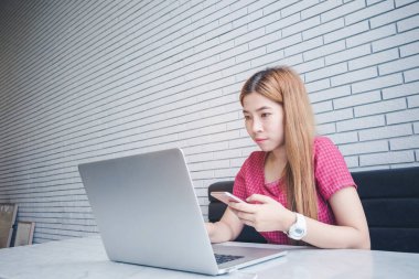 Asyalı kız cep telefonu ile oturup bir kahve dükkanında çalışan bir