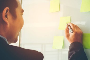 Post-it üzerinde yeni iş planlama fikirleri koyarak işadamı