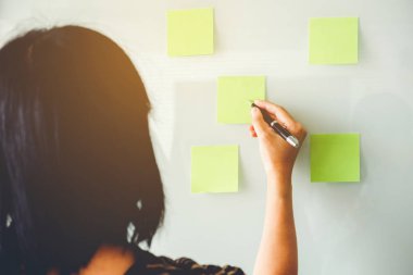 Post-it üzerinde yeni planlama fikirleri koyarak girişimci kadın 