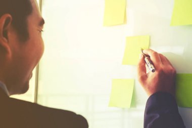Post-it üzerinde yeni iş planlama fikirleri koyarak işadamı