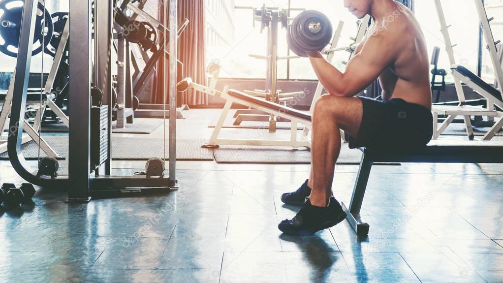 Muscular Man built athlete working out in gym sitting on weightl