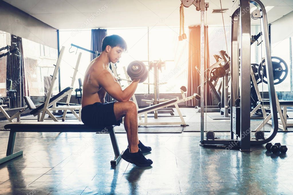 Muscular Man built athlete working out in gym sitting on weightl