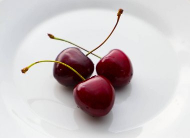 Beyaz bir plaka üzerinde üç kiraz meyve. Kiraz olgun lezzetli fru