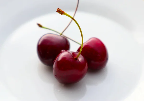 Beyaz bir plaka üzerinde üç kiraz meyve. Kiraz olgun lezzetli fru — Stok fotoğraf