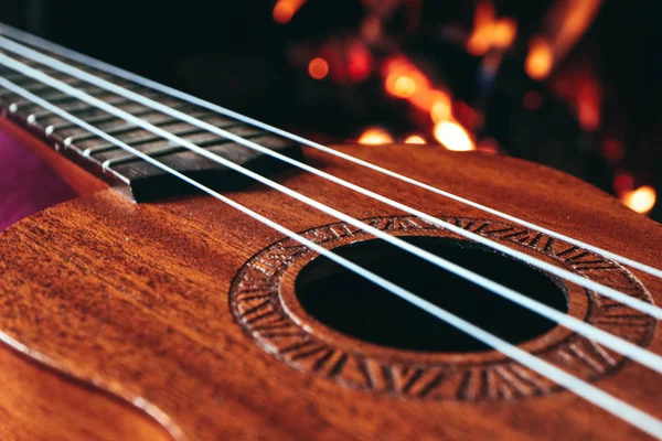 Ukulele small guitar close up stings, fireplace on the backgroun