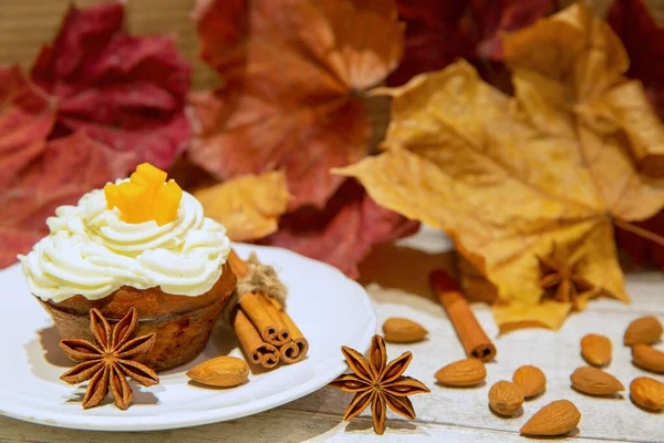 Sweet pumpkin cupcake with cinnamon and nuts on colorful autumn leaves background. Fall dessert.