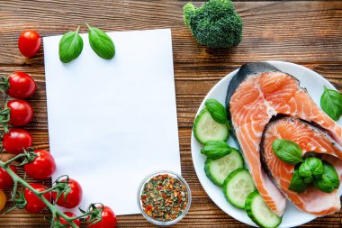  Kağıt defter ve yemek malzemeleri ahşap masa, üst manzara. Çiğ somon ve sebze. Diyet kavramı. 