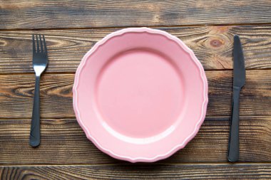 Kahverengi ahşap arka planda boş pembe tabak. Masa ayarı, çatal bıçak takımı, üst görünüm. 