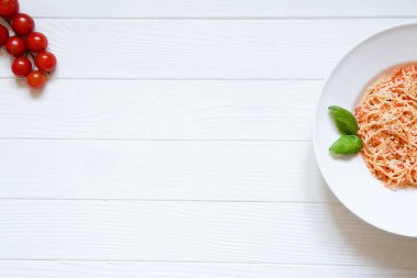 Domates makarnası peynir, fesleğen, kırmızı kiraz domatesleri ve beyaz ahşap arka planda fesleğen yaprağı. Lezzetli İtalyan mutfağı, en güzel manzara. Parmesanlı, ahşap kaplamalı spagetti. Boşluğu kopyala. 