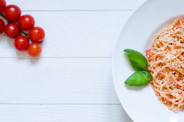 Domates makarnası peynir, fesleğen, kırmızı kiraz domatesleri ve beyaz ahşap arka planda fesleğen yaprağı. Lezzetli İtalyan mutfağı, en güzel manzara. Parmesanlı, ahşap kaplamalı spagetti. Boşluğu kopyala. 