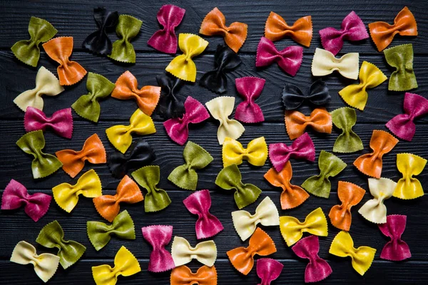 Renkli farfalle çeşitleri ya da ahşap kırsal siyah arka planda farfalline. İtalyan mutfağı. Pembe, yeşil, kırmızı, mor, sarı ve turuncu. 