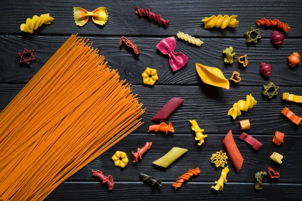 Siyah arka planda farklı türde makarna. Sarı conchiglie, renk farfalline, turuncu domates spagetti, ping, yeşil ve mor. 