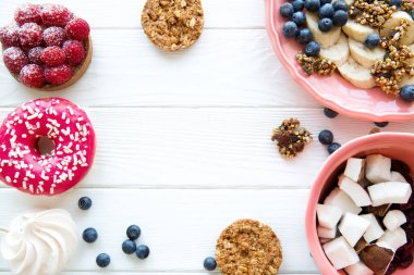 Masa servisi, sağlıklı kahvaltı: taze yaban mersinli ve muzlu granola. Beyaz ahşap masada mercan renkli tabakta hindistan cevizi parçaları. Metin için boşluk. 