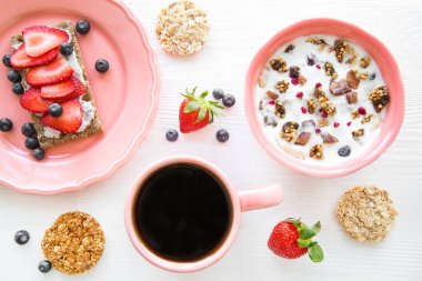 Kahvaltıda granola, böğürtlen ve çilekli yoğurt. Bir fincan sade kahve, üst manzara. Parlak renkler. Lezzetli sağlıklı atıştırmalık. 