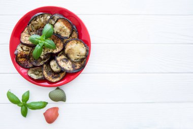 Ahşap masa arka planında kırmızı tabakta ızgara patlıcan. Boşluğu kopyala, metin için boş alan. Yeşil yapraklar ve koni süslemeleri. 