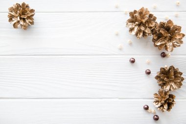 Altın çam kozalakları (boyanmış köknar kozalakları) kahverengi boncuklar ve bej boncuklar ile beyaz rustik arka plan, üst görünüm, kopyalama alanı. Noel arkaplanı, selamlama yeri. 