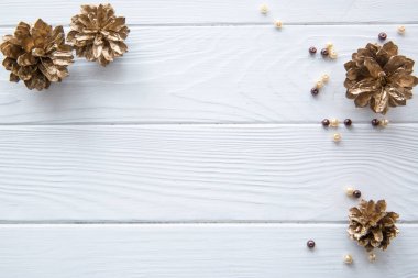 Beyaz ahşap masa zemininde altın kozalaklar. Bej boncuk süslemeleri. Metin için boş alan. 