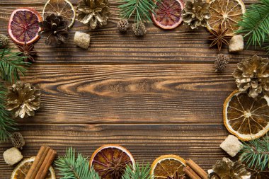 Kurumuş portakallar, altın koniler ve baharatlı Noel arkaplanı. Kahverengi ahşap arka planda anason yıldızlı esmer şeker ve tarçın çubukları. Mesaj için yer var. Üst görünüm. 