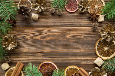 Kurumuş portakallar, altın koniler ve baharatlı Noel arkaplanı. Kahverengi ahşap arka planda anason yıldızlı esmer şeker ve tarçın çubukları. Mesaj için yer var. Üst görünüm. 