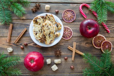 Geleneksel Noel pastası. Kahverengi ahşap masa arkasında Alman bayramı tatlısı. Kırmızı elmalar, tarçın çubukları, kurutulmuş portakal dilimleri dekorasyonu. Ateş ağacı dalları. 