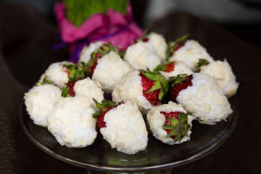 Çilekler kaplanmış beyaz çikolata ve siyah tabakta badem taneleri. 