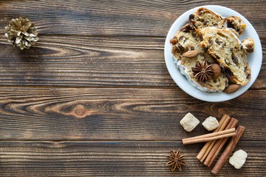 Geleneksel Noel pastası dilimi, tarçın çubukları, kaş şekeri ve anason yıldızları baharatları. Kahverengi masa zemininde altın koniler. Metin için boş alan. Uzayı kopyala Üst görünüm. 