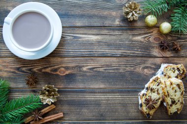 Kahverengi ahşap masa zemininde Noel pastası olan bir fincan sıcak çikolata. Firavun ağacı dalları, altın toplar ve çam kozalakları, metin için boş alan. Boşluğu kopyala. 