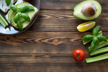 Avokado, krem peynirli sandviç ve kahverengi masada fesleğen yaprağı. Mesaj için yer var. Metin için boş alan. 