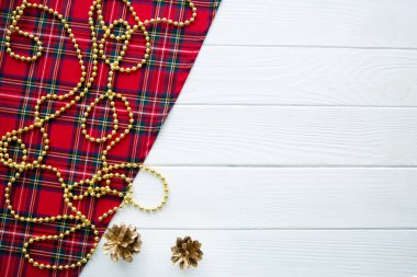 İskoç geleneksel kumaşı, altın Noel dekoru, beyaz ahşap masa zemininde altın kozalaklar. Üst Manzara. Metin için boş alan. Boşluğu kopyala. 