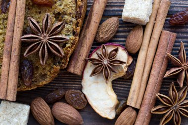 Fındıklı, bademli ve kuru üzümlü bir dilim Noel pastası. Tarçınlı çubuk baharatlar, anason yıldızları ve şeker yakın çekim. Makro, üst manzara. Kış havası. 