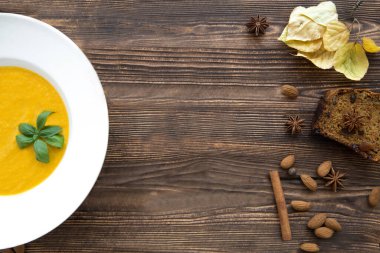 Lezzetli balkabağı kremalı çorba, baharat ve soğanla harmanlanmış. Uzayı kopyala, üst görünüm. Sonbahar havası, sarı yapraklar ve havuçlu kek. Kahverengi rustik ahşap arkaplan. 