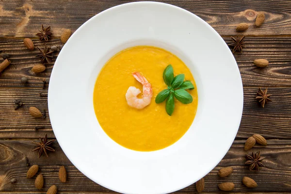 Tasty pumpkin cream soup with shrimps and basil leaves, blended with spice and carrots. Top view. — Stock Image Tasty Pumpkin Cream Soup Shrimps Basil Leaves Blended Spice Carrots Royalty Free Stock Photos