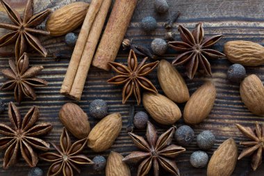Noel baharatı: tarçın çubukları, anason yıldızları, badem fıstıklı tüm baharatlar, makro, kahverengi ahşap arka planda yakın plan, üst görünüm. 
