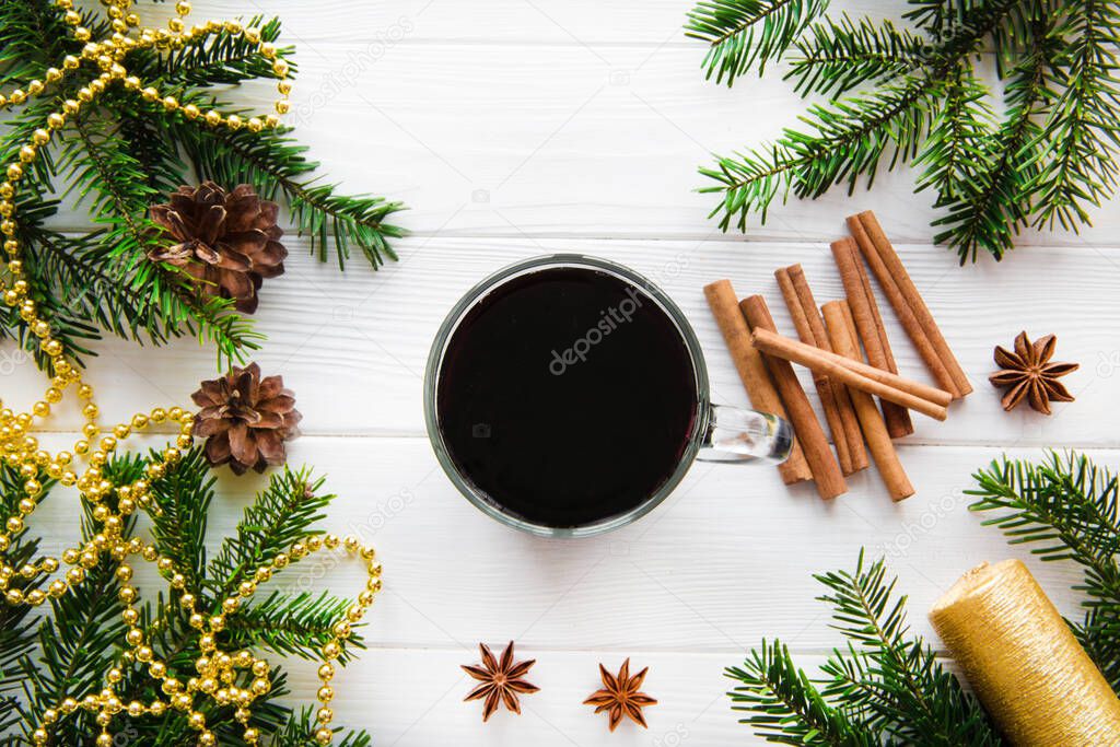 A cup of hot aromatic mulled wine with spices, golden christmas decoration on white table, top view. Aromatic winter drink. 
