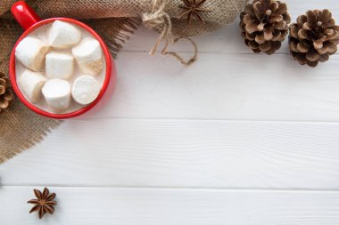 Sıcak çikolata ve marşmelovlu Noel bardağı. Sütlü sıcak kakao, anason, beyaz ahşap arka planda koni süslemesi, Hessian üst manzarası. Boşluğu kopyala. 