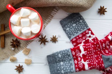 Sıcak çikolata ve marşmelovlu Noel bardağı. Yılbaşı süsleri ve geyikli çoraplar. Sütlü, anasonlu ve tarçınlı sıcak kakao, beyaz ahşap arkaplanlı boncuklar, üst manzara. 