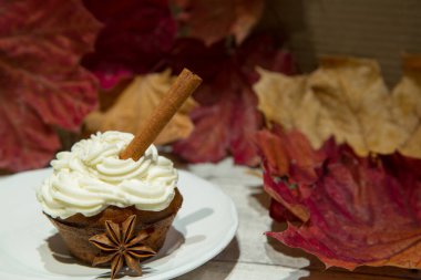 Tarçın çubuklu balkabağı baharatlı kek ve anason süslemesi. Sonbahar baharatlı ev yapımı, balkabaklı, krem peynirli ve ahşap arka planda sarı ve kırmızı yapraklı kremalı kekler.. 