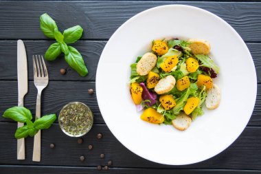 Bitki ve fesleğen yapraklı balkabağı salatası. Siyah ahşap masada sonbahar havası yiyeceği. Üst görünüm. 